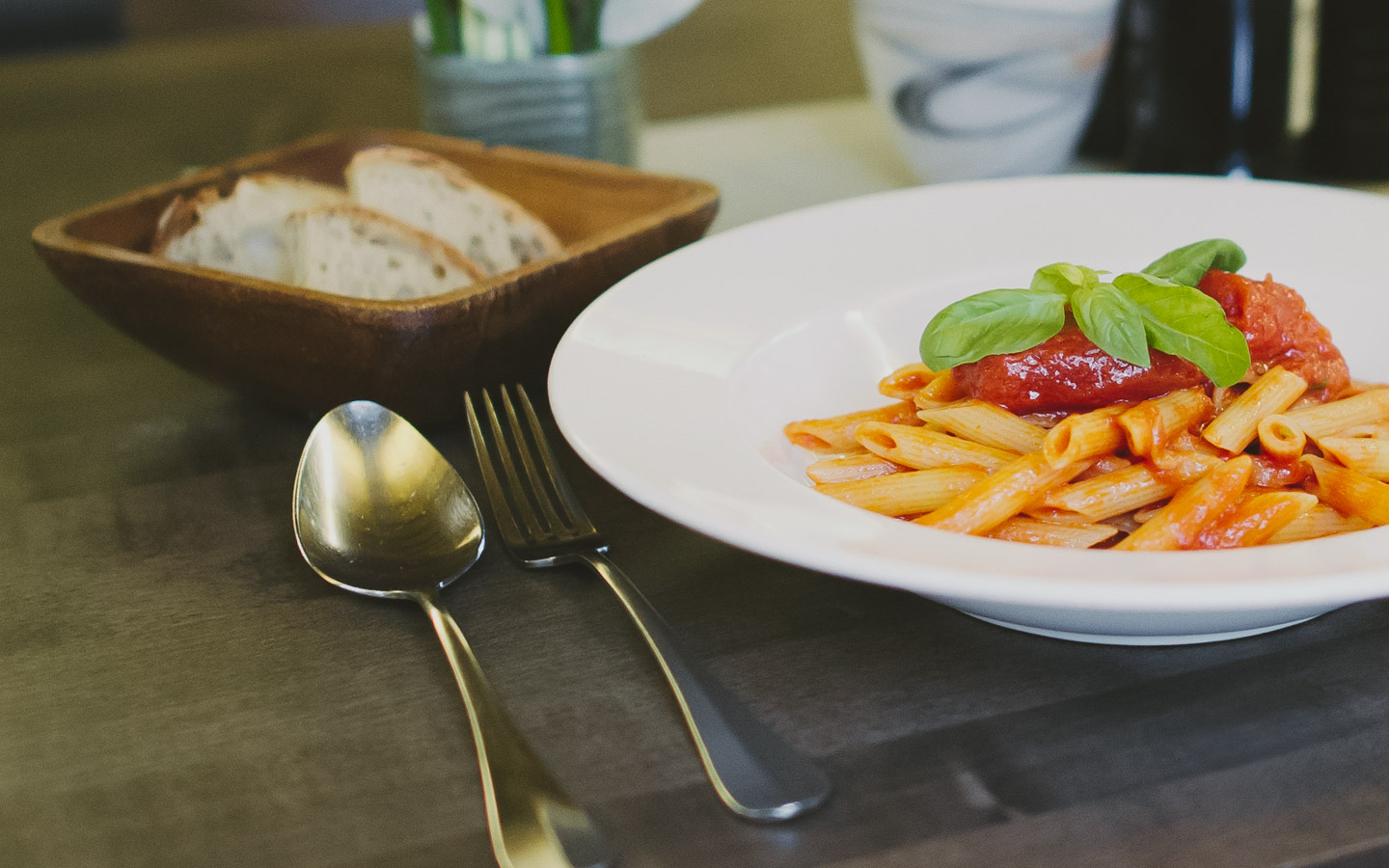 Aufnahme eines Tellers mit Pasta. Links oben im Bild steht ein Körbchen mit Brot.