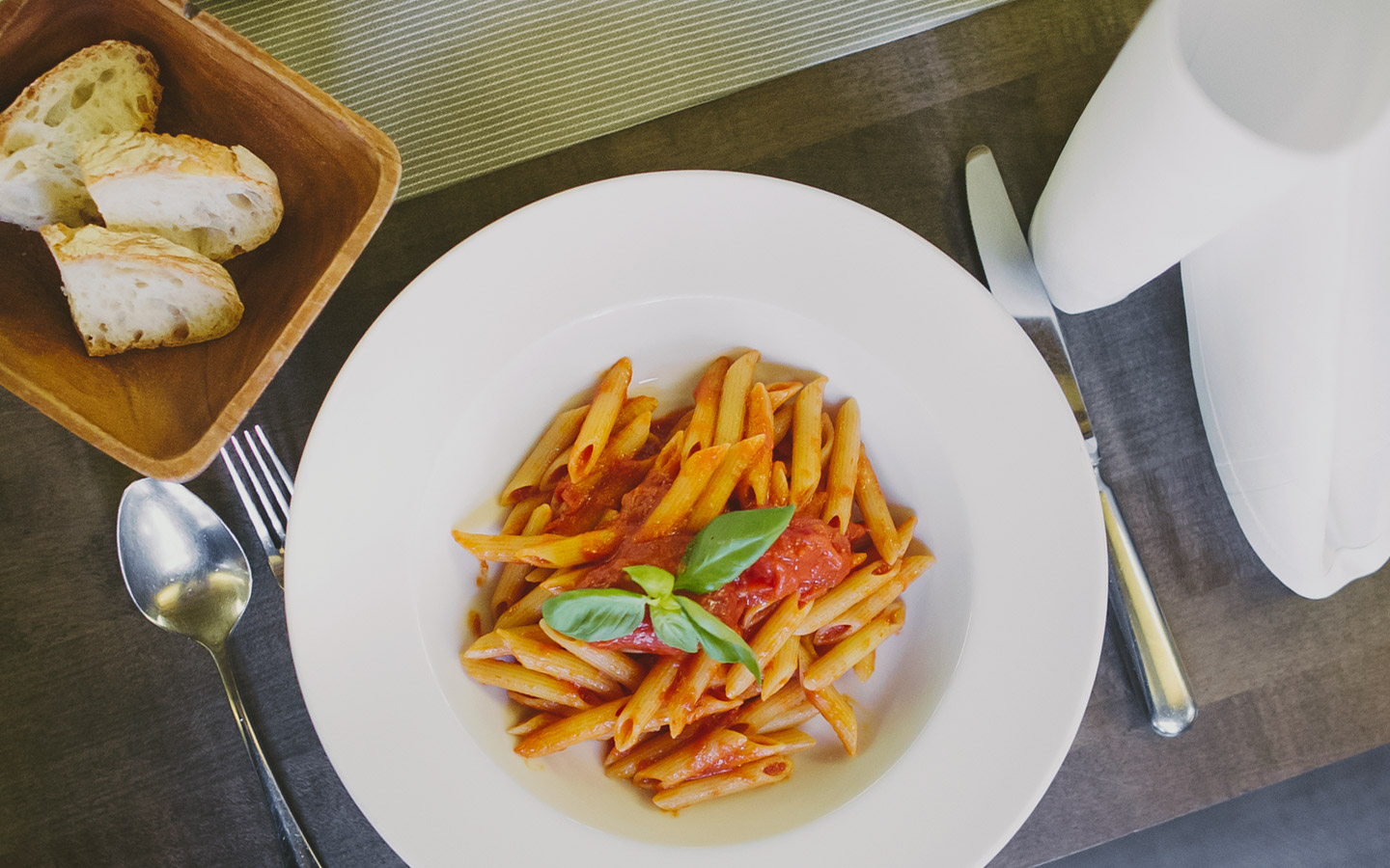 Aufnahme eines Tellers mit Pasta. Links oben im Bild steht ein Körbchen mit Brot.