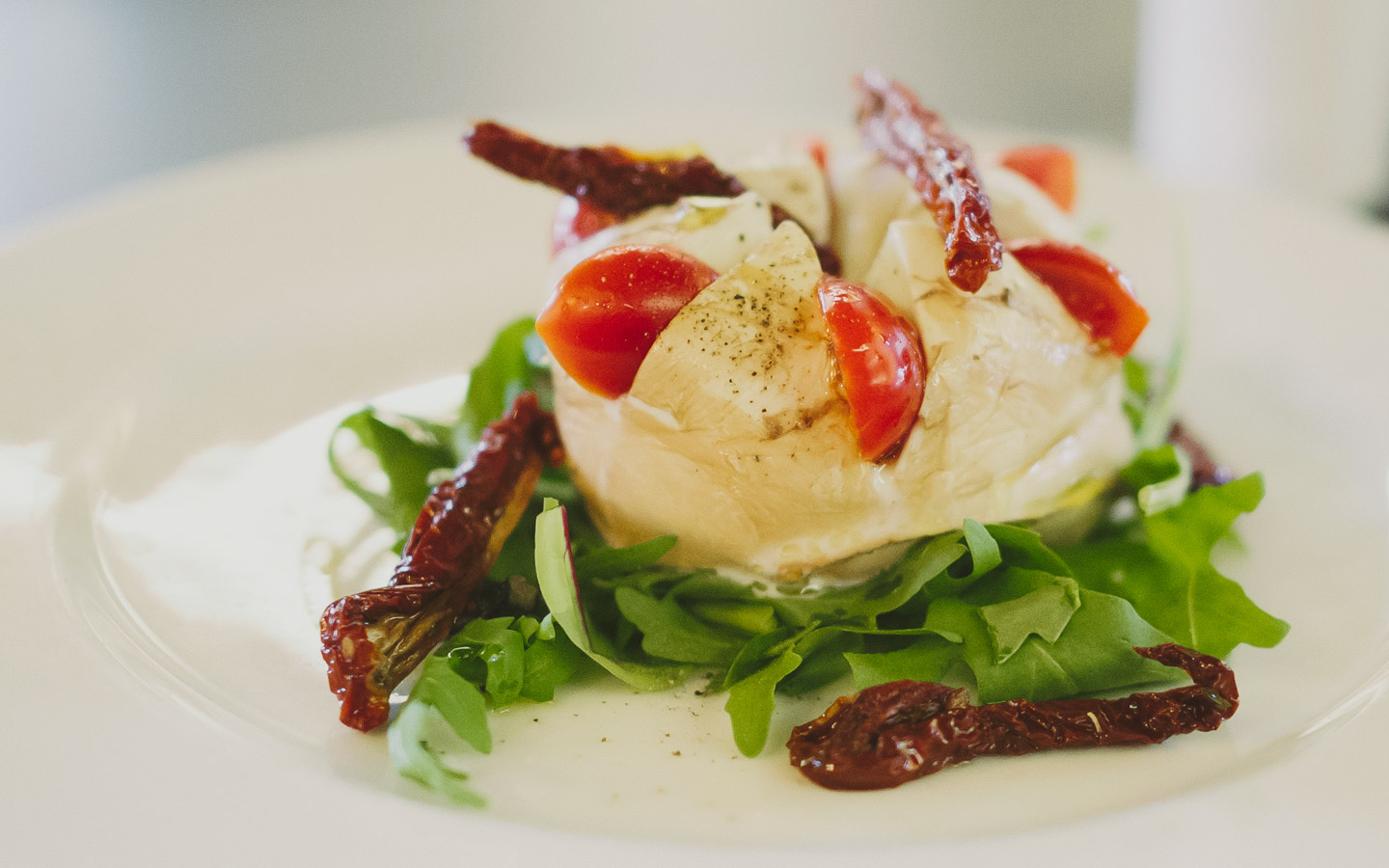Ein schön angerichteter Mozarella der mit Tomaten dekoriert ist und auf einem Bett aus Rucola liegt.